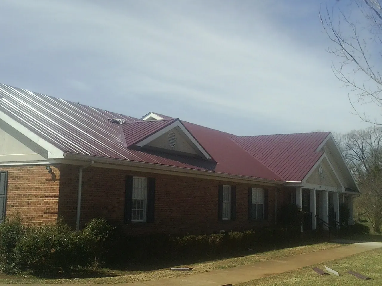 Red metal roof with gabled entries on a long brick building, from a Hail Damage Roof Repair job in Clarks Mills
