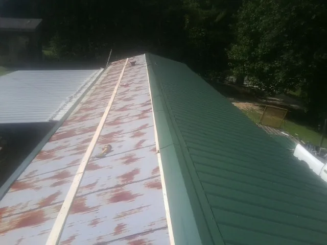 Old rusted panels beside newly installed green metal roofing — Wind Damage Roof Repair by Roofing Brothers in Clarks Mills