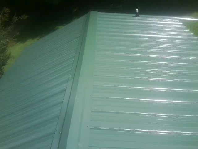 New green metal panels meeting at the ridge of a roof — Flat Roof Repair work by our crew in Clarks Mills