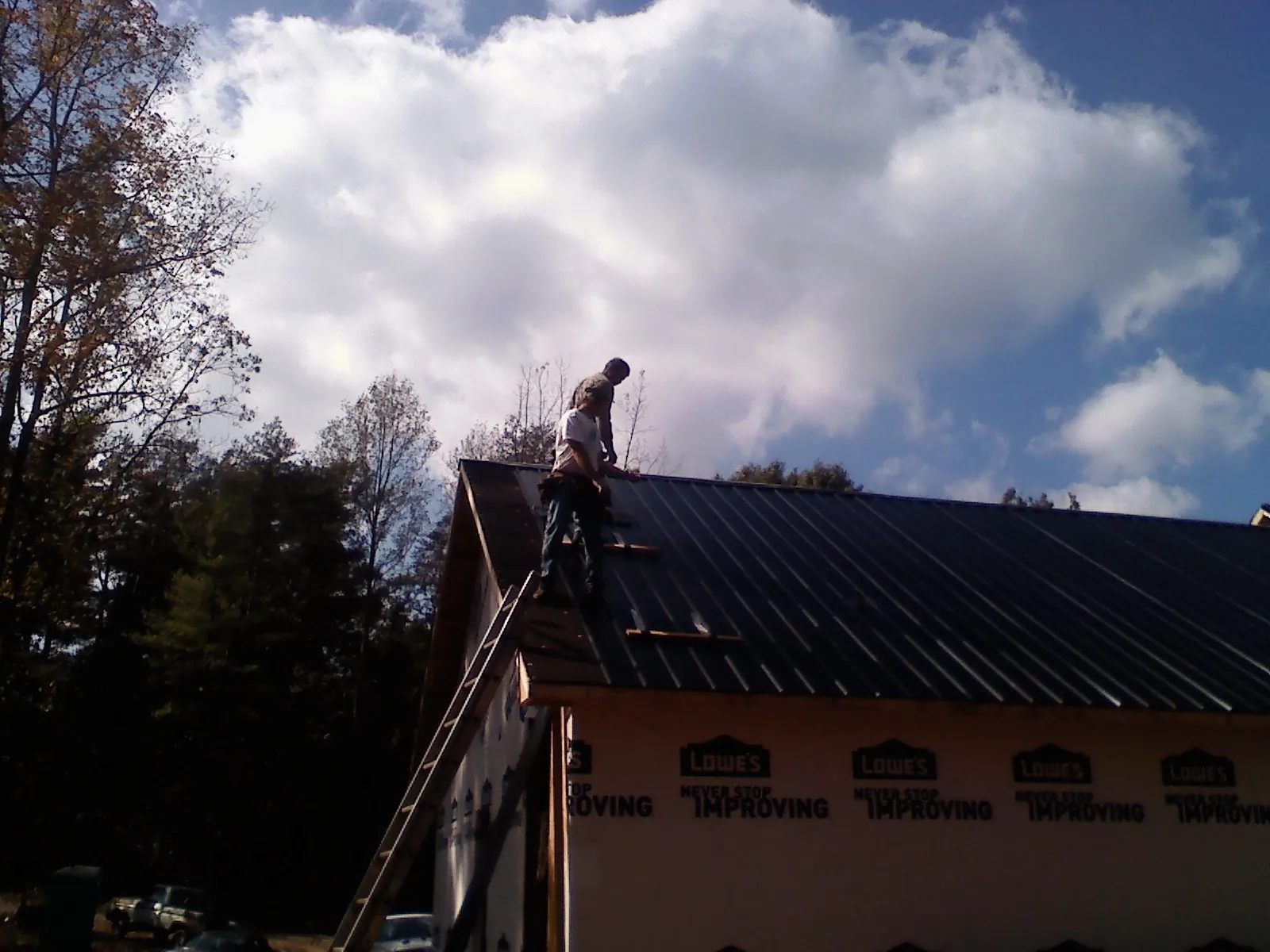 Roofer fastening dark metal panels high against a cloudy sky, from a Roof Inspection job in Clarks Mills