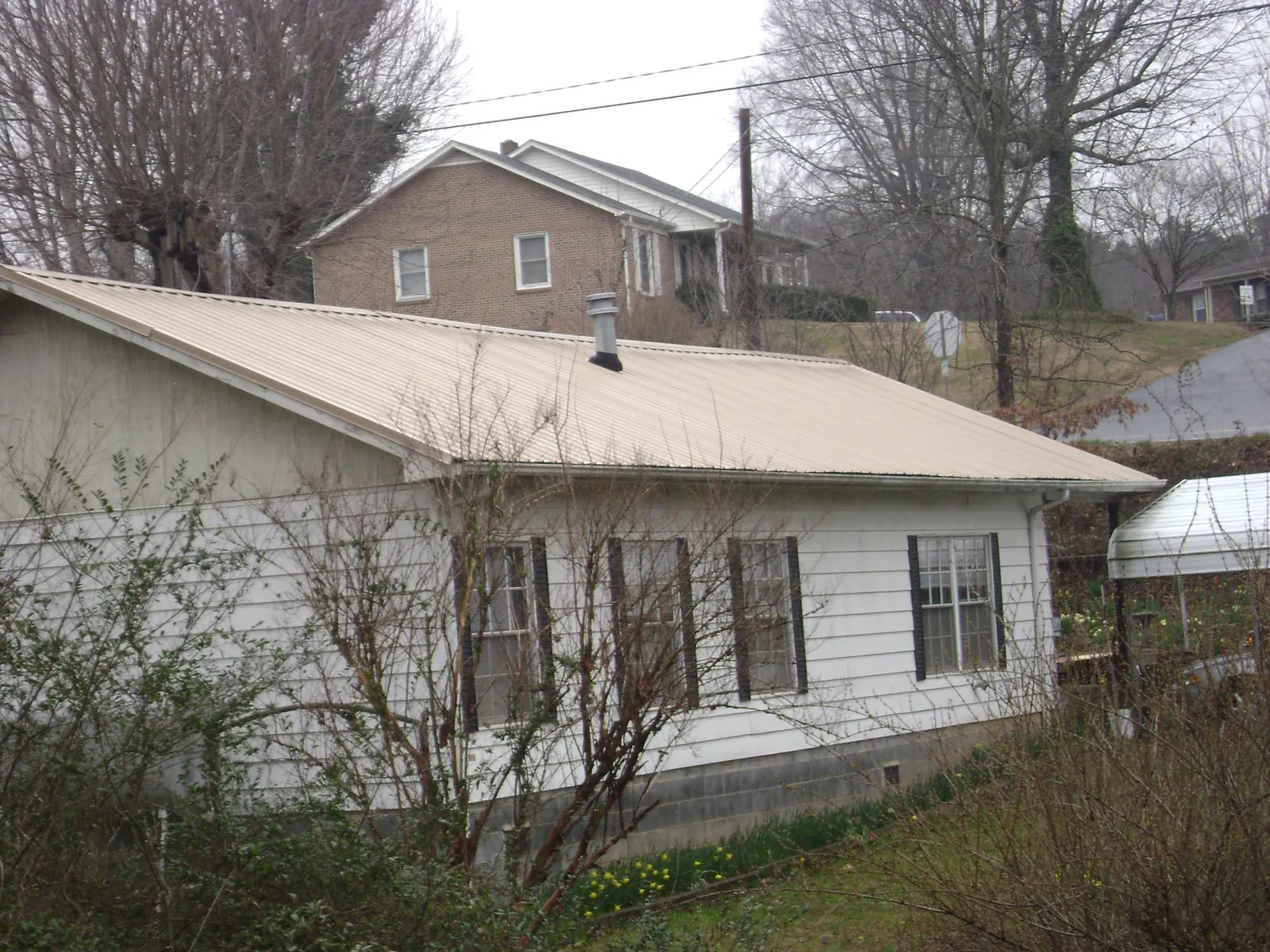 Tan metal roof on a white sided house set into a hillside — Commercial Roofing by Roofing Brothers in Clarks Mills