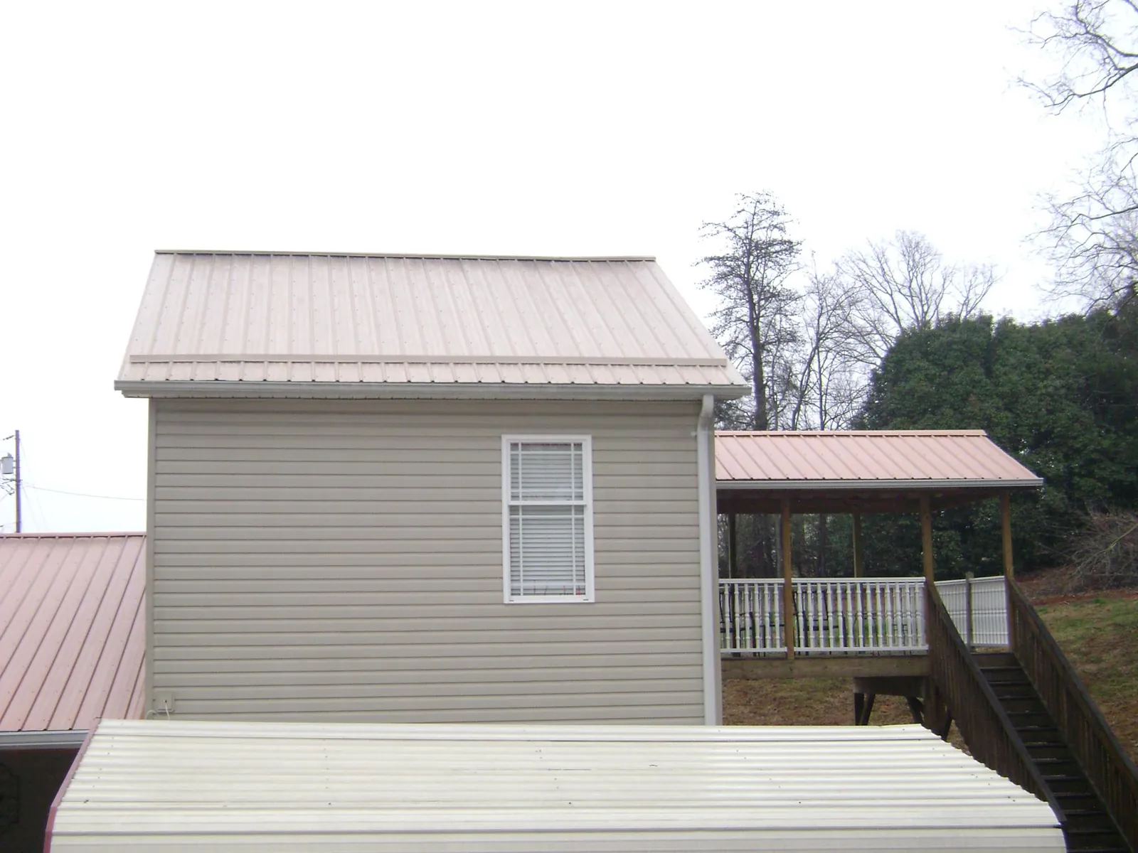 Tan metal roofs on a two story addition and attached porch, from a Roof Replacement job in Clarks Mills